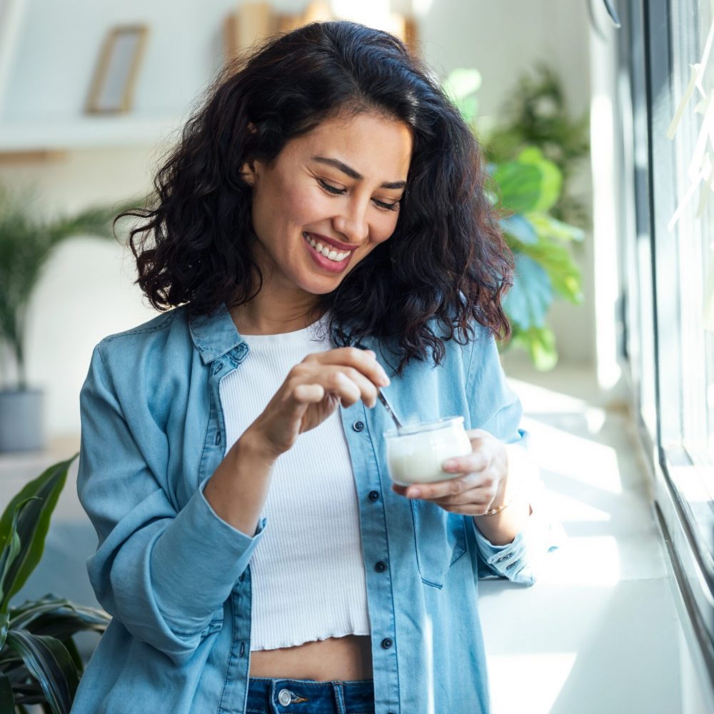 Shot,Of,Happy,Beautiful,Woman,Eating,Yogurt,While,Standing,In